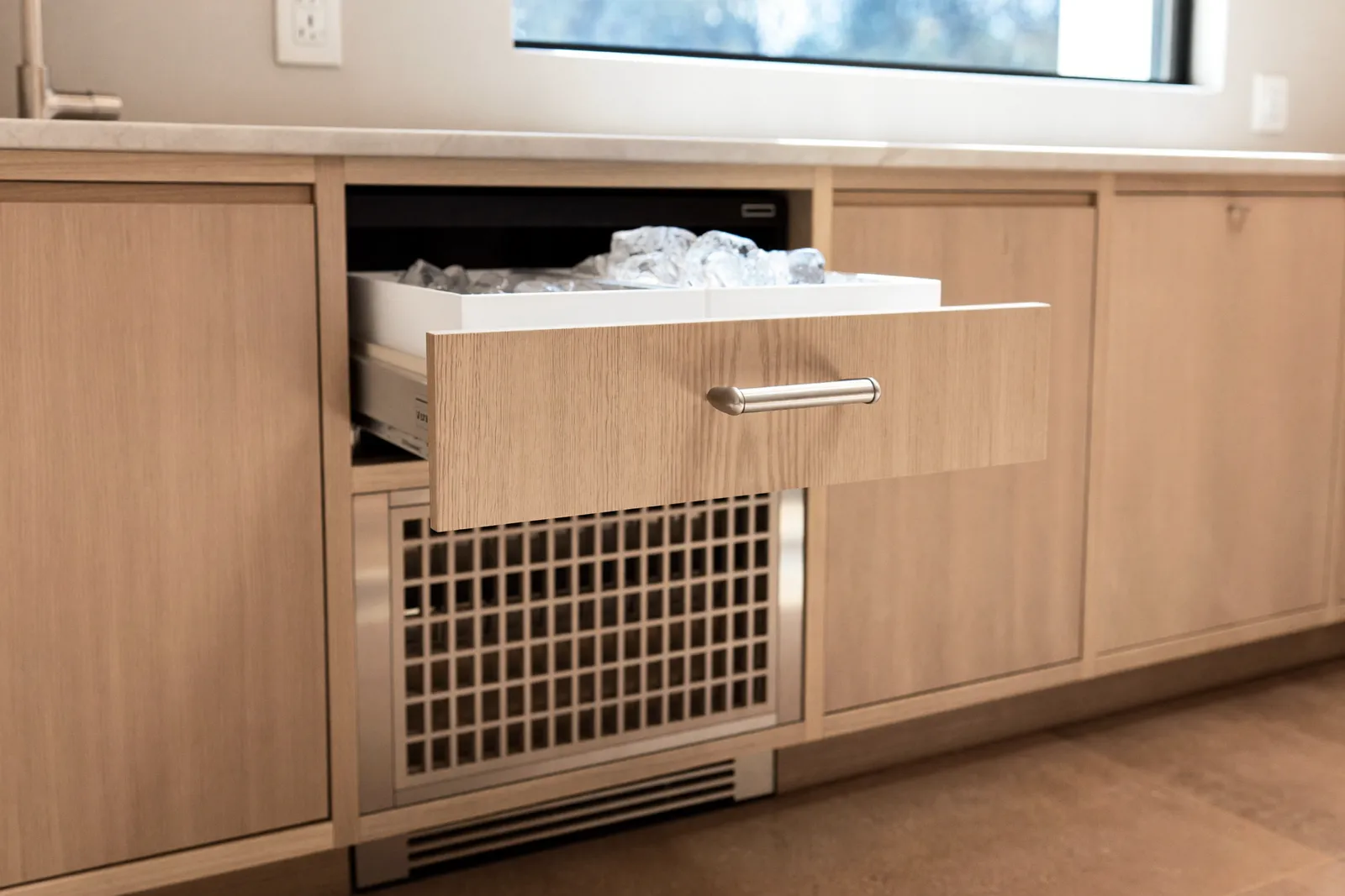 An open undercounter ice maker drawer filled with ice cubes
