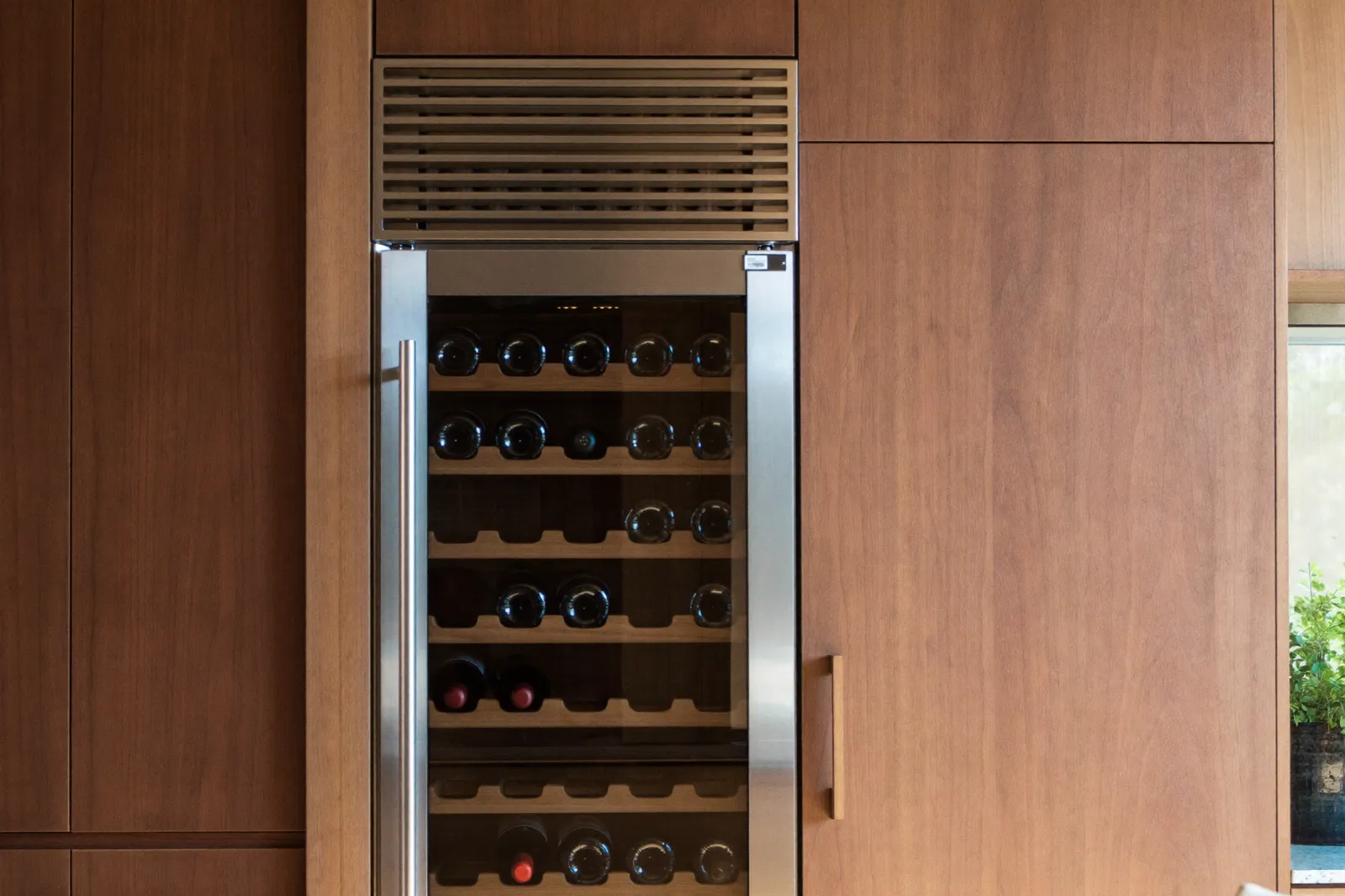 A built-in dual-zone wine cooler with bottles on wooden cradle shelves